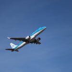 A blue and white airplane ascends into a clear sky.