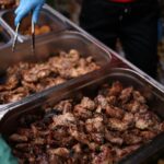 Close-up of grilled meat being served with tongs at a street food stall.