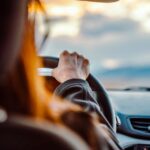 Close-up van de hand van een vrouw op het stuur tijdens het rijden met een schilderachtig uitzicht voor zich.