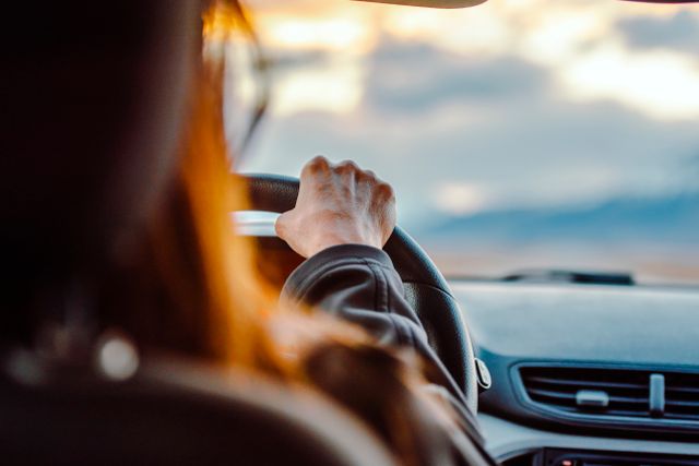 Close-up van de hand van een vrouw op het stuur tijdens het rijden met een schilderachtig uitzicht voor zich.